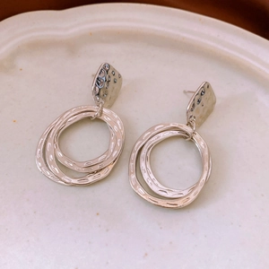 Close-up of silver geometric hoop earrings with hammered texture on a ceramic plate