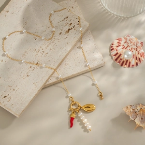 Detailed shot of gold pearl necklace with shell and red pepper charms on stone