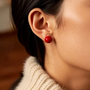 Close-up of a model wearing a glossy red spherical stud earring with vintage pearl style