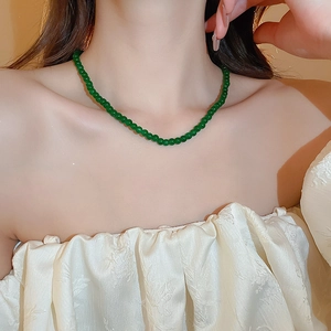 Gros plan du collier de perles vert émeraude porté par un mannequin au style épuré