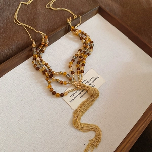 Detail of multi-layer crystal beaded necklace with golden chain tassels on a linen tray