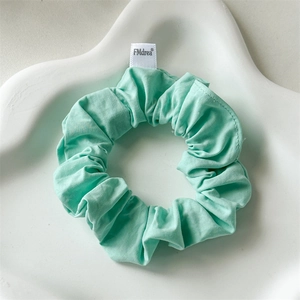 Detail of light mint green cotton scrunchie with soft pleated texture on a white tray