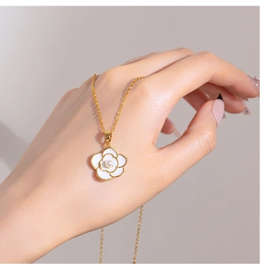 Detailed view of the gold chain and white enamel camellia pendant with a pearl inlay