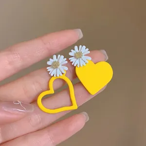 Detail of handmade yellow daisy and heart asymmetric earrings held in a hand