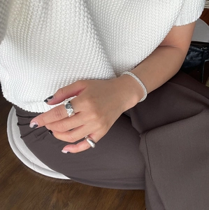 Macro view of sterling silver rings and braided bracelet on model wearing knitwear
