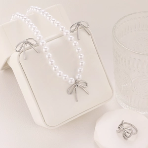 Detailed set of silver bow jewelry featuring white pearl necklace and matching earrings