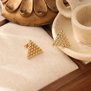 Close-up of golden triangular heart stud earrings on elegant ceramic display