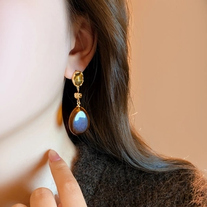Gros plan de boucles d'oreilles élégantes en résine marron ambre avec reflet bleu sur modèle