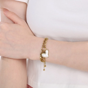 Detail eines goldenen Herz-Armbands mit Perleneinlage und hängenden Tasseln am Handgelenk