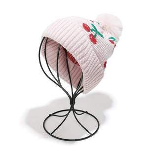 Close-up of pink knit beanie featuring cherry patterns and a fluffy pom-pom detail