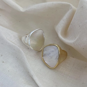 Detailed close-up of organic shell inlay silver and gold rings on beige linen texture