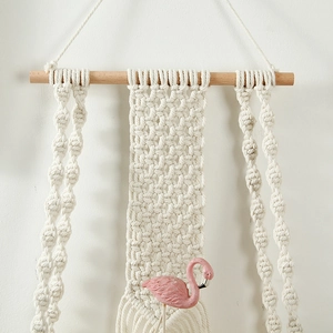 Detail of hand-woven macrame wall shelf featuring creamy white cotton rope and tassels