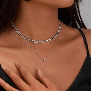 Close-up of layered 925 silver Cuban chain and zircon letter A pendant on neck