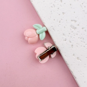 Detailed view of peach-shaped hair clips with pink fruit and mint green leaves