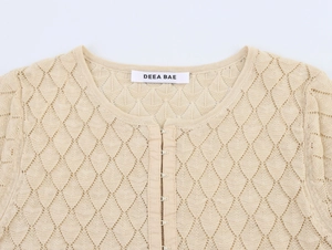 Detail of beige knit cardigan featuring diamond crochet pattern and metal hook closure