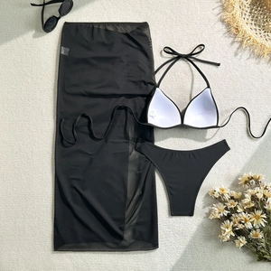 Flat lay of a black three-piece bikini set with a long mesh sarong and summer accessories