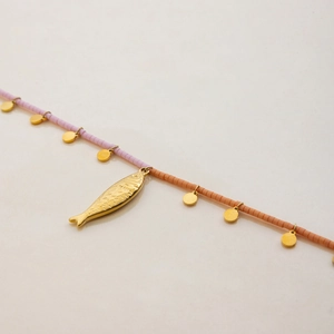 Close-up of golden fish pendant and coral beads on a minimalist stainless steel necklace