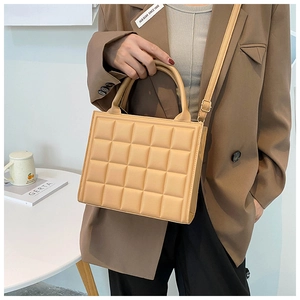 Detail of a khaki quilted square handbag held by a model in a warm lifestyle setting