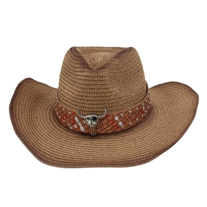 Close-up of western straw cowboy hat featuring metal bull skull ornament and woven band