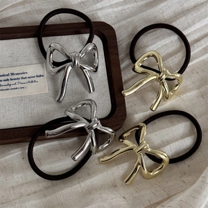 Set of 4 gold and silver metal bow hair ties on elegant wooden tray and knit fabric