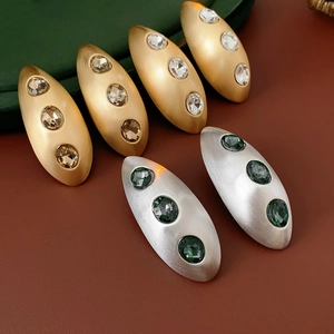 Detail of matte oval earrings with brushed texture and inlaid gemstones on leather base