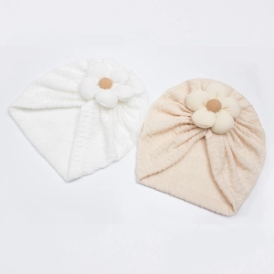 Detail of knitted baby turban hats in white and beige with large 3D fabric flower