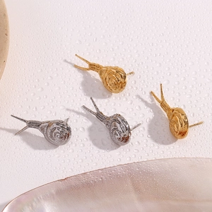Macro shot of snail-shaped gold and silver earrings on a pearl shell with water drops