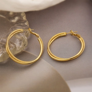 Detail of twisted gold C-shaped hoop earrings with textured and polished finish