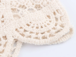 Macro detail of cream crochet knit fabric showing intricate hollow floral patterns and texture