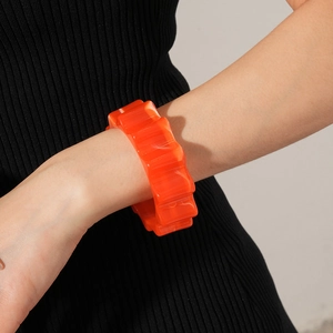Polished bright orange resin wave bangle worn on wrist with black knit sleeve contrast