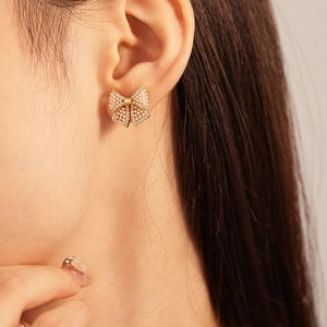 Elegant gold bow earrings with imitation pearls and sparkling zircon on model's ear