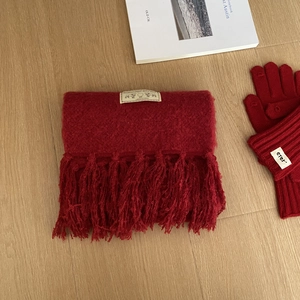 Bufanda de punto roja con flecos y guantes a juego sobre suelo de madera natural