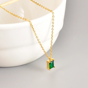 Detail of square emerald pendant on gold-plated stainless steel chain over a white ceramic bowl