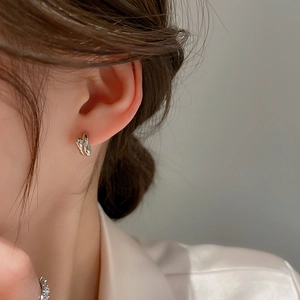 Close-up of a silver twist knot hoop earring worn by a model in a minimalist style