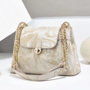 Detail of macaron beige crossbody bag featuring golden chain and marble grain texture