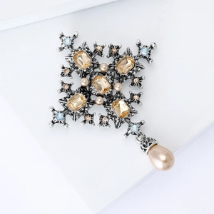 Detailed view of silver baroque cross brooch with champagne gems and pearl drop