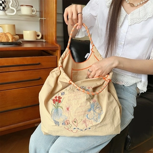 Détail de la broderie florale sur un sac fourre-tout beige à anses tissées