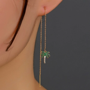 Macro detail of gold-plated palm tree earrings featuring sparkling green zircons