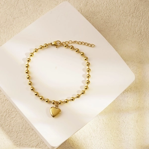 Gold beaded bracelet with heart pendant and adjustable clasp on white display