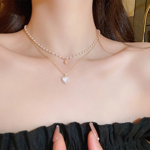 Gros plan du collier doré double rang avec perles et pendentif cœur sur la clavicule