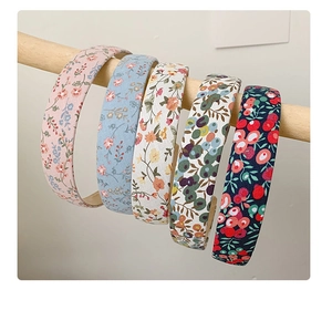 Detailed display of five floral fabric headbands in various colors hanging on a wood bar