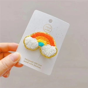 Detail of plush rainbow hair clip with embroidery on white handmade packaging card