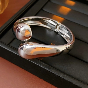 Detail eines silbernen metallischen Tropfen-Armreifs in einer schwarzen Schmuckschatulle