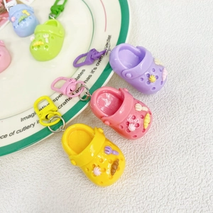 Top view of five colorful mini clog shoe keychains with cartoon charms on a white tray