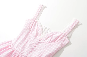 Detail of pink plaid dress featuring lace straps and front button decorations on white backdrop