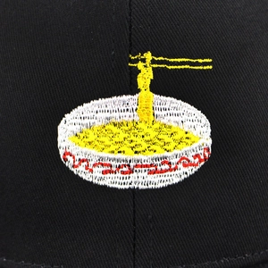 Close-up of colorful ramen bowl embroidery on black cotton twill baseball cap fabric