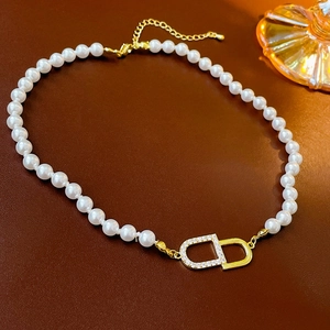 Détail macro du fermoir doré avec logo CD sur un collier ras du cou en perles blanches