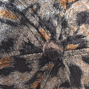 Macro shot of gold leopard jacquard fabric and top button detail on the baseball cap