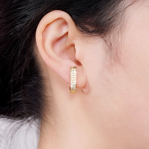 Close-up of a gold huggie hoop earring with pave white stones on a model ear