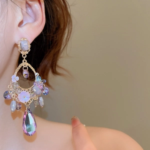 Close-up of elegant gold earrings featuring purple teardrop crystals on a female model
